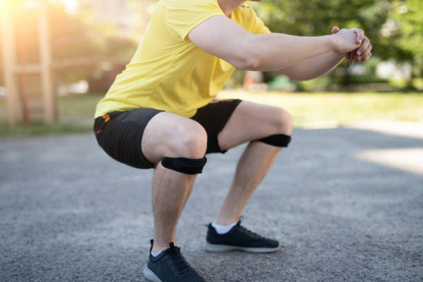 A man doing a squat with a knee support bandage in a modern gym.